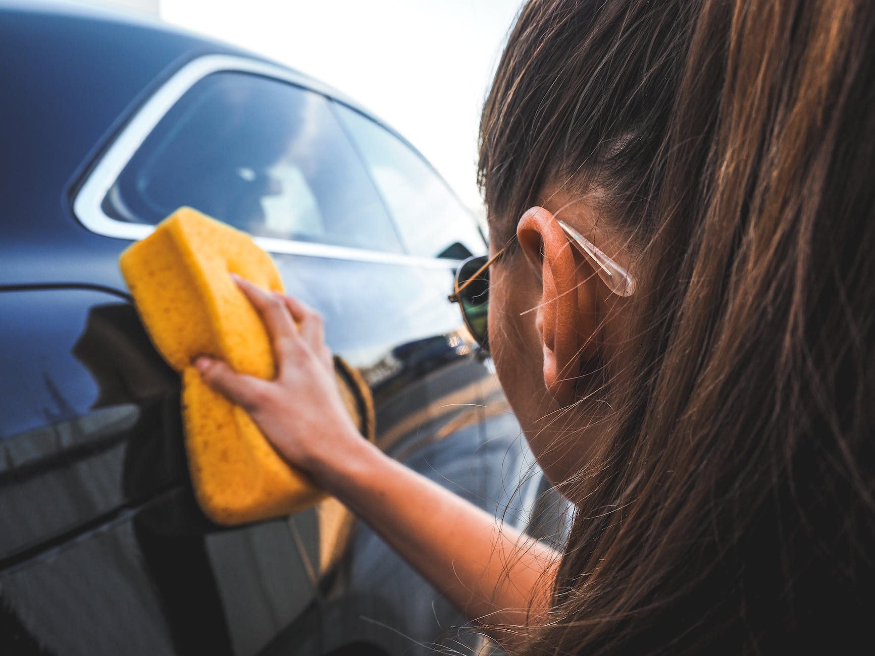 woman wiping the car with yellow sponge, living from paycheck to paycheck