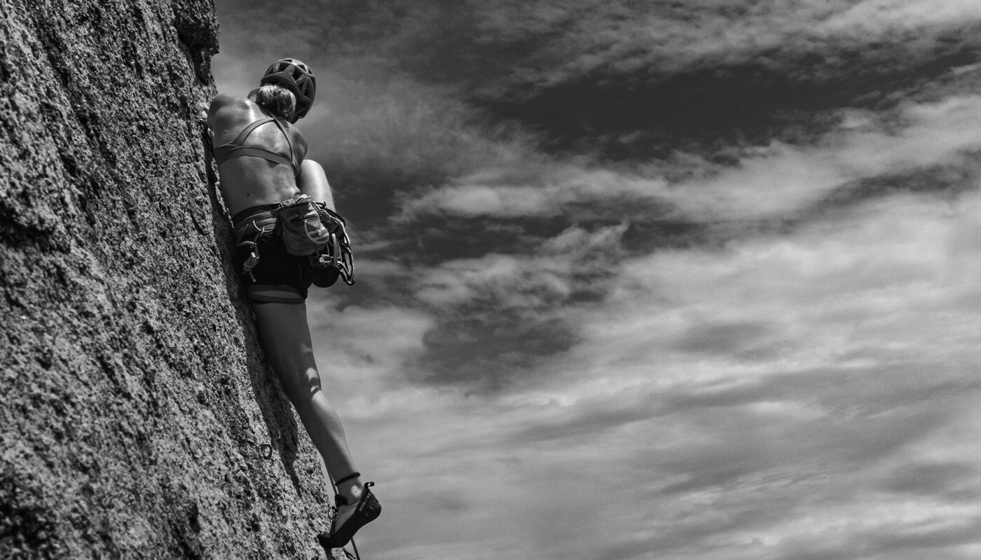 woman rock climbing under clouds in black and white