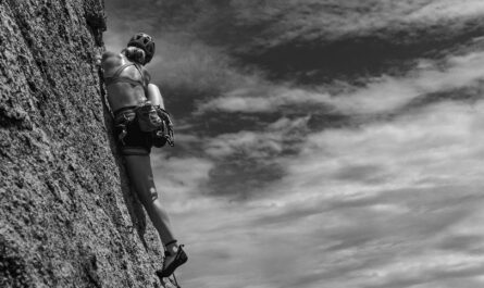 woman rock climbing under clouds in black and white