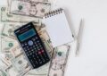 calculator and notepad placed over stack of paper bills