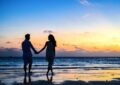 man and woman holding hands walking on seashore during sunrise