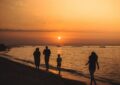 silhouette of people walking on seashore during sunset